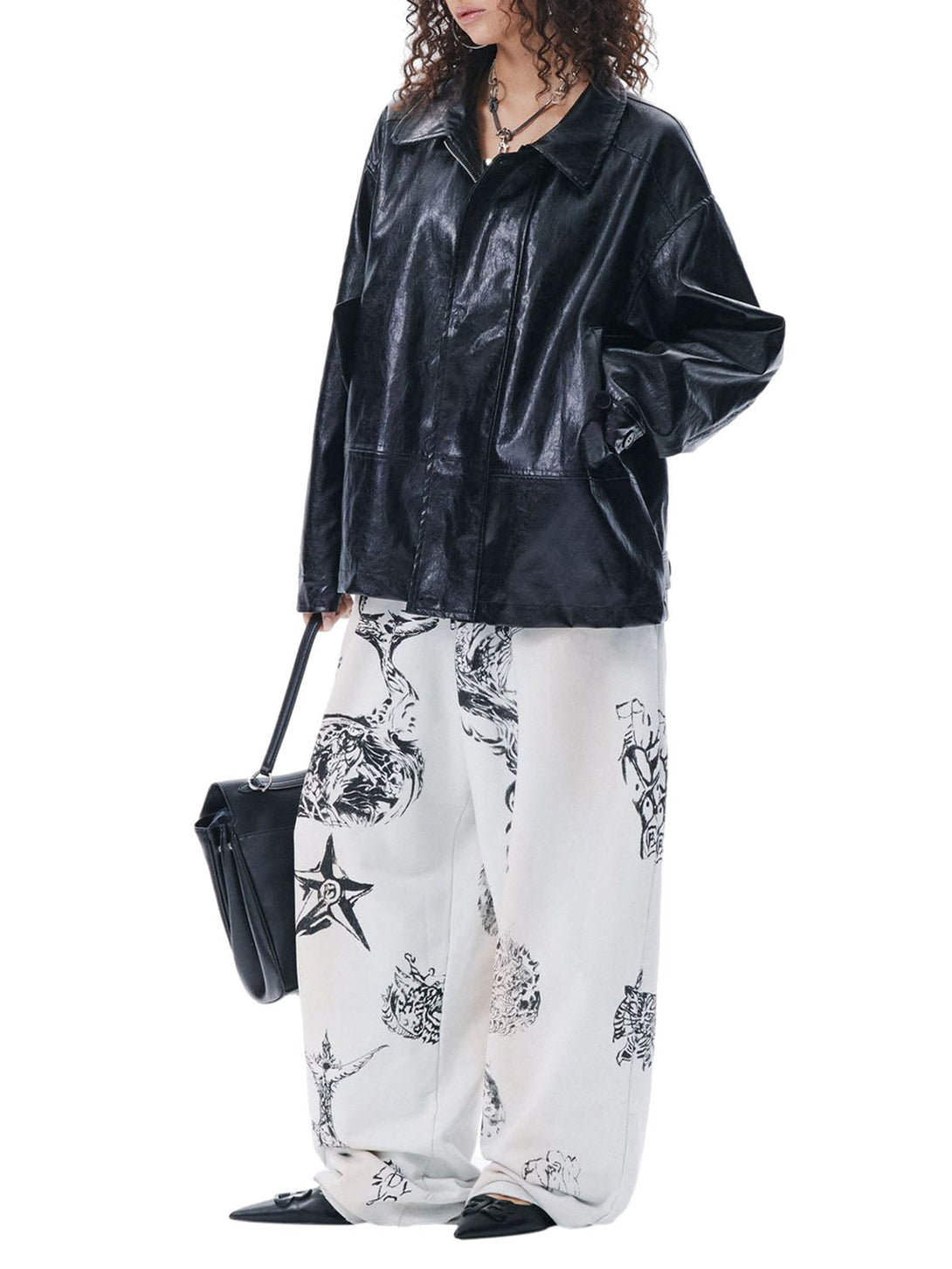 Person wearing a black leather jacket and white pants with black floral pattern on a white background