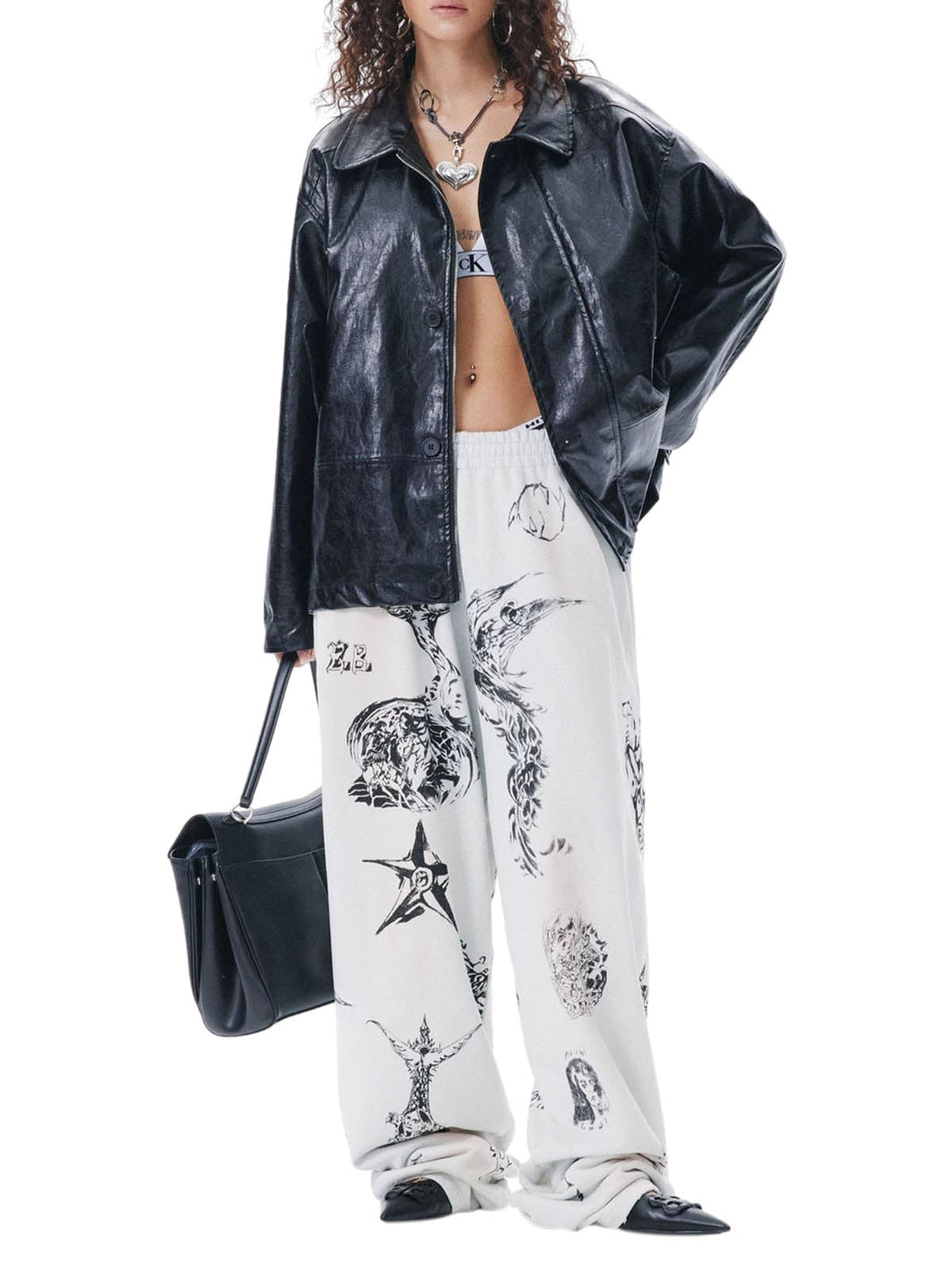 Person wearing a black leather jacket and white pants with black patterns, holding a black handbag.