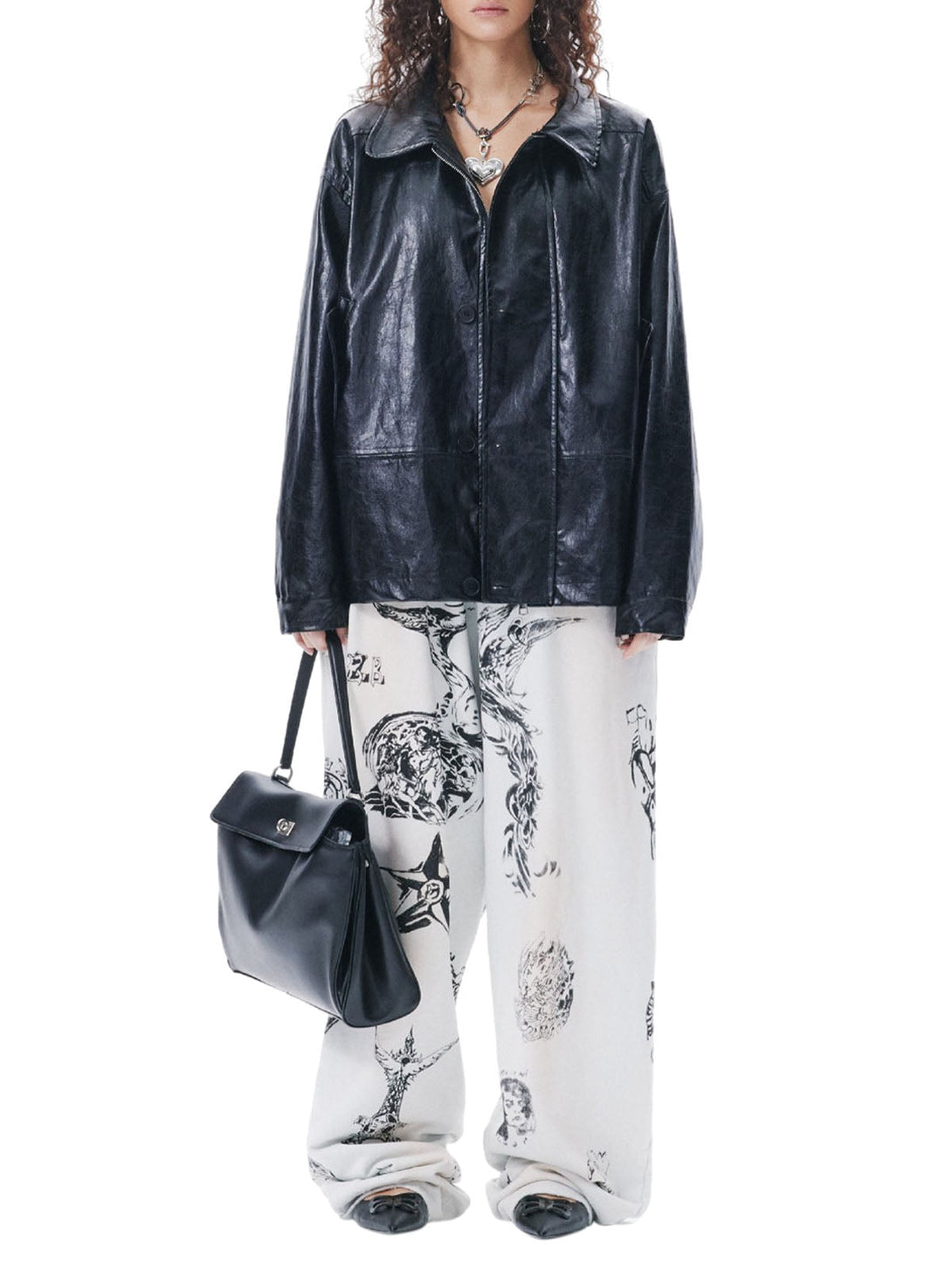 Person wearing a black leather jacket and white pants with black patterns, holding a black handbag on a white background.