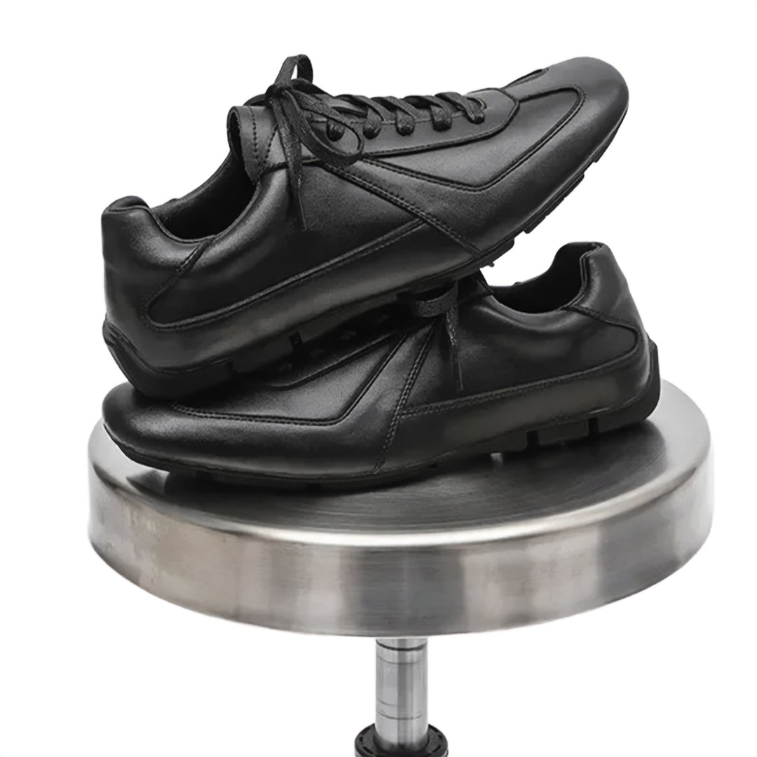 Black leather shoes on a metallic stand against a white background