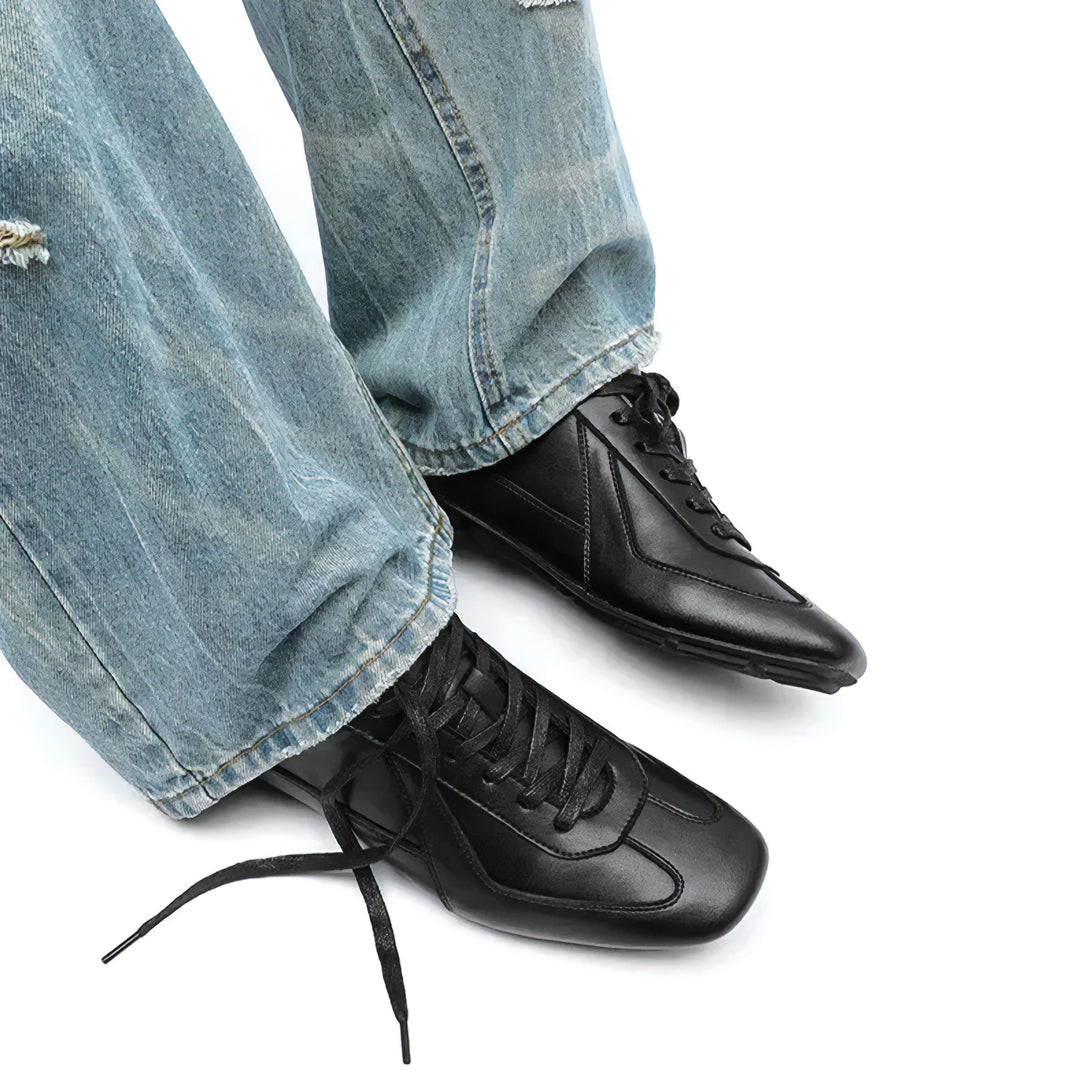 Black shoes worn with blue jeans on a white background