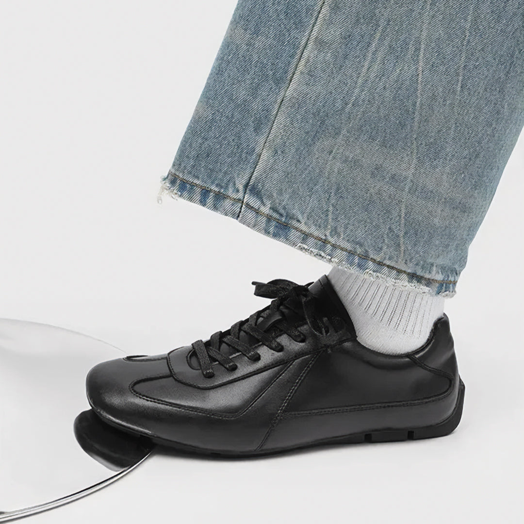 Black sneaker worn with light blue jeans and white socks on a neutral background