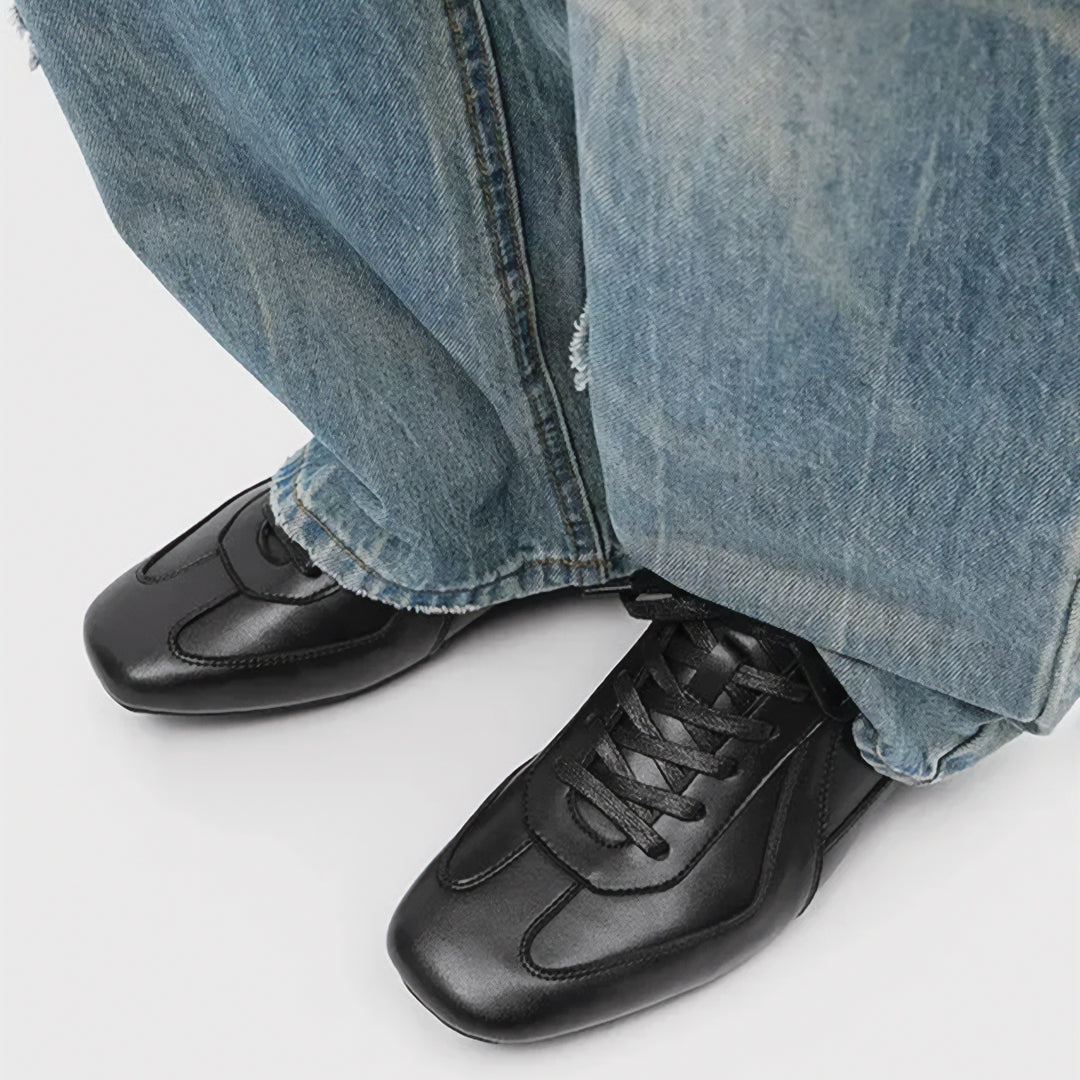 Black leather shoes worn with blue jeans on a white background