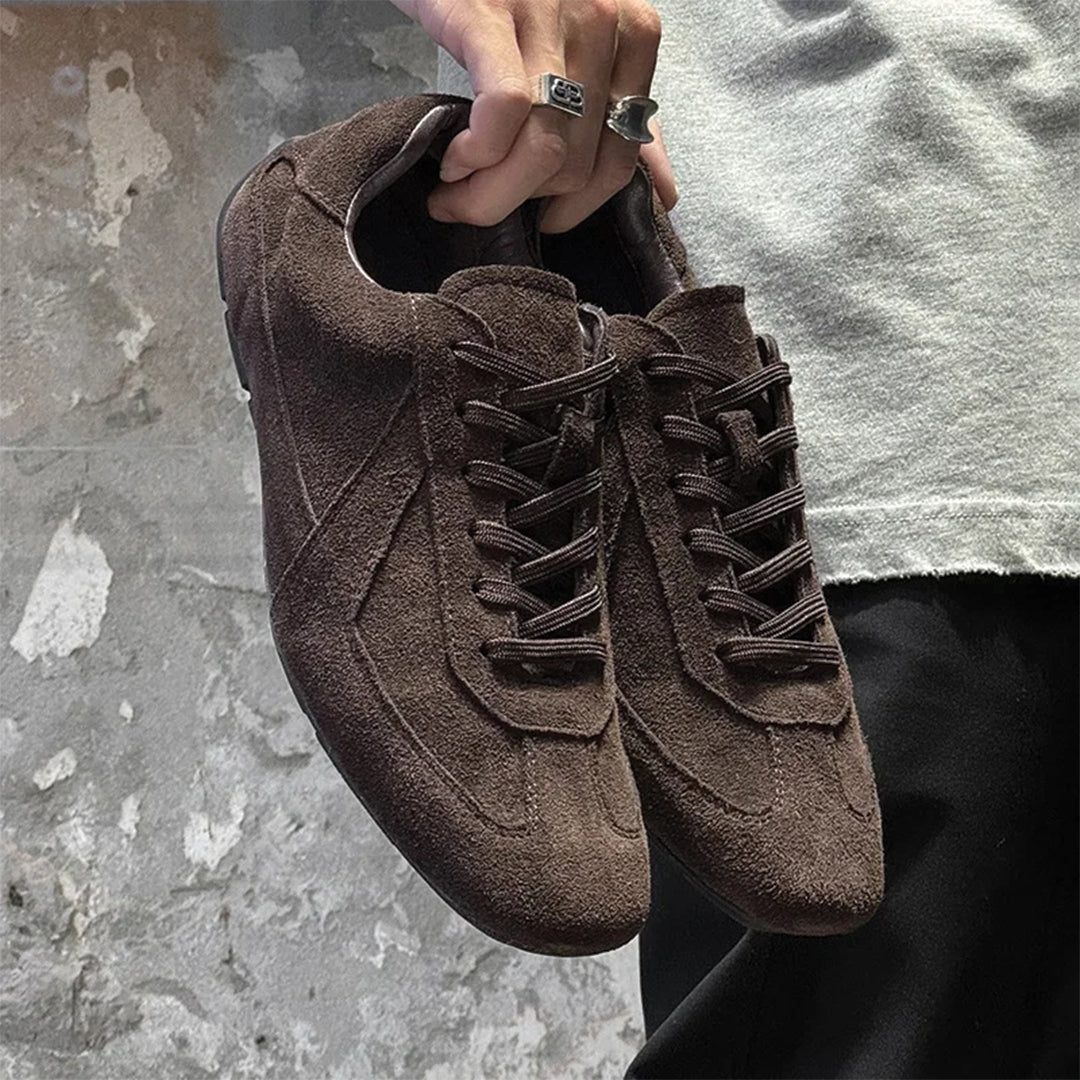 Brown suede shoes held by a person against a textured gray background