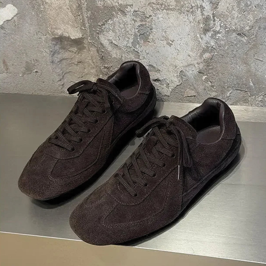 Pair of brown suede shoes on a metallic surface with a stone wall background
