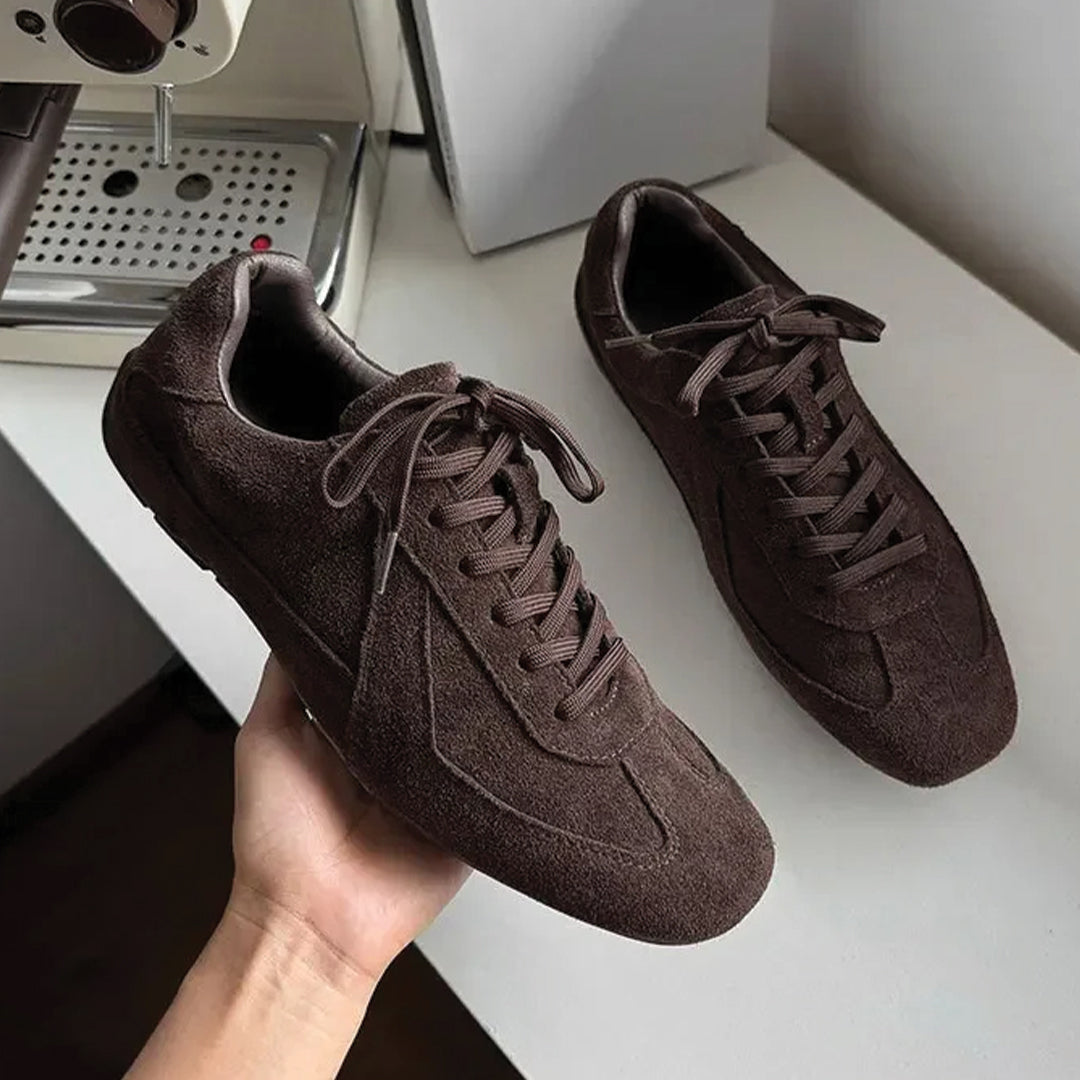 Brown suede sneakers on a white surface with a coffee machine in the background