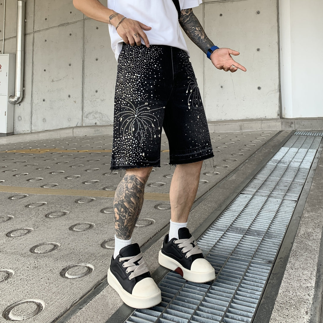 Person wearing black shorts with white embellishments and black sneakers on a concrete floor.
