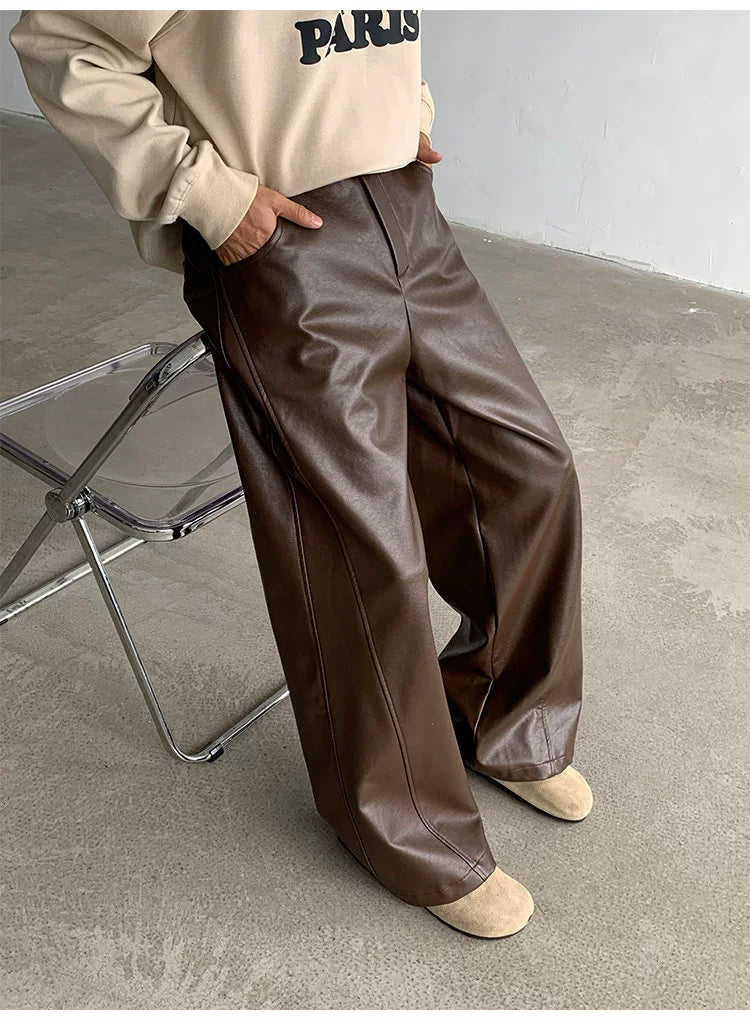 Person wearing a beige sweatshirt with 'PARIS' text and brown leather pants sitting on a clear chair.