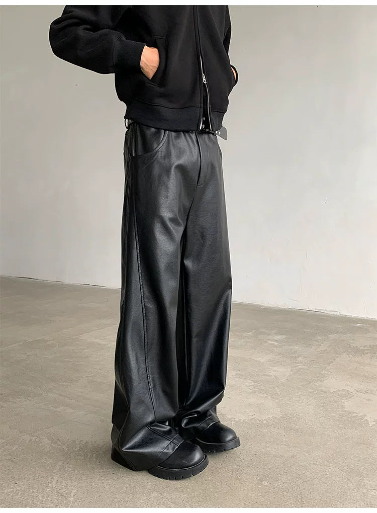 Person wearing black leather pants and shoes against a plain background