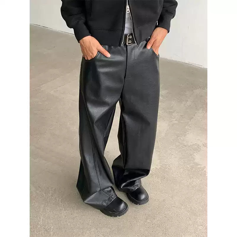 Person wearing black leather pants and shoes on a plain background